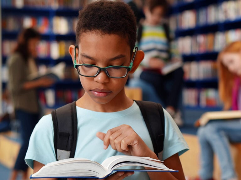 Young boy with glasses reading book in the library