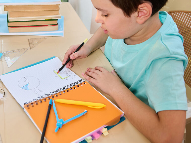 Boy doing geometry homework in notebook with compass and pencils