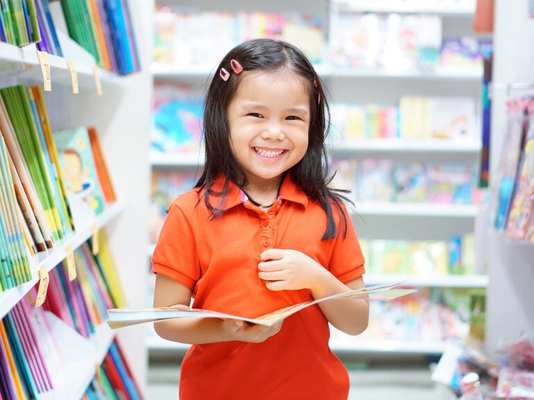 Kindergarten girl standing in library smiling holding a book