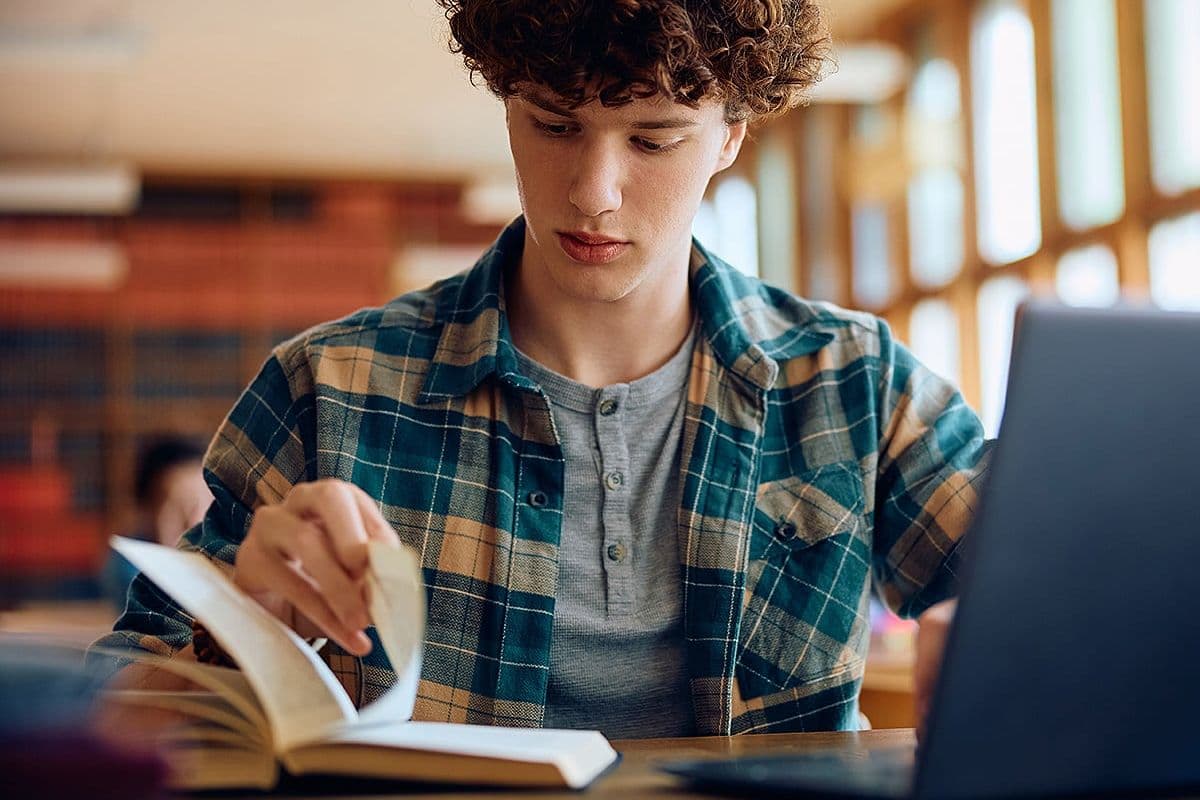 Male student reading book at school library