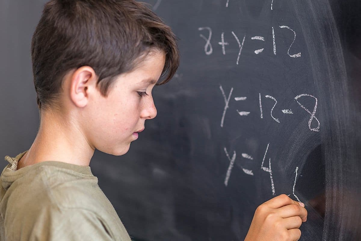 Male student solving algebra problem on a blackboard.