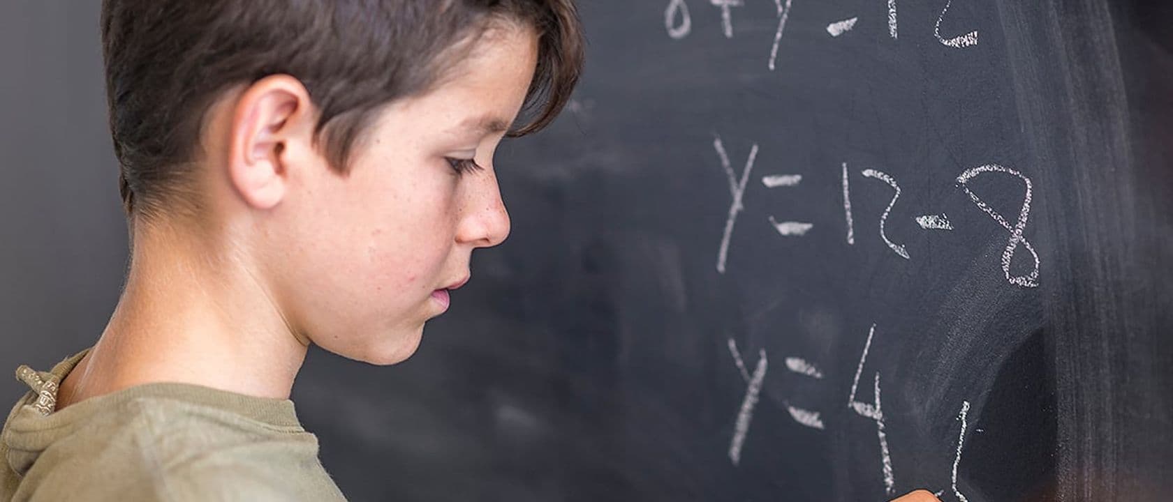 Male student solving algebra problem on a blackboard.