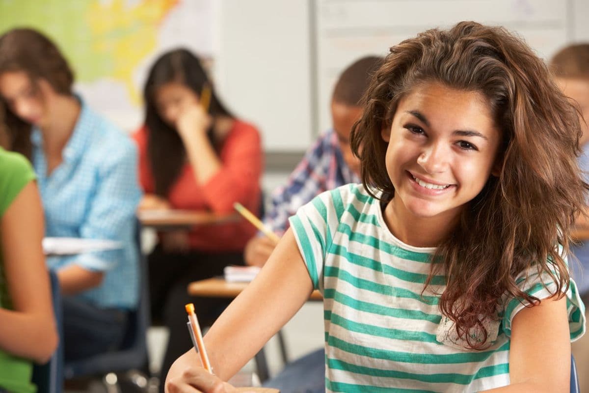 Portrait Of Female Pupil Studying At Desk In Classroom Smiling At Camera
