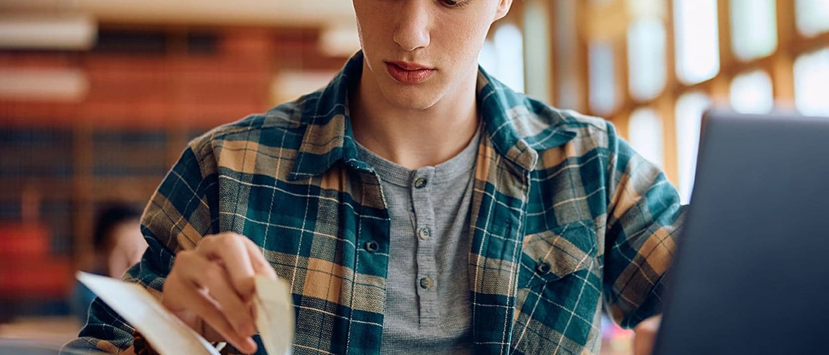 Male student reading book at school library
