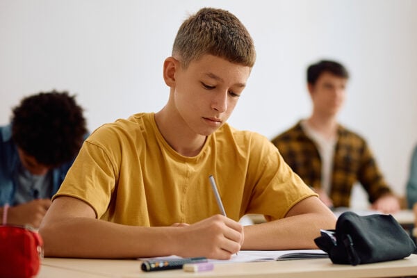 Male high school student writing in notebook in classroom.