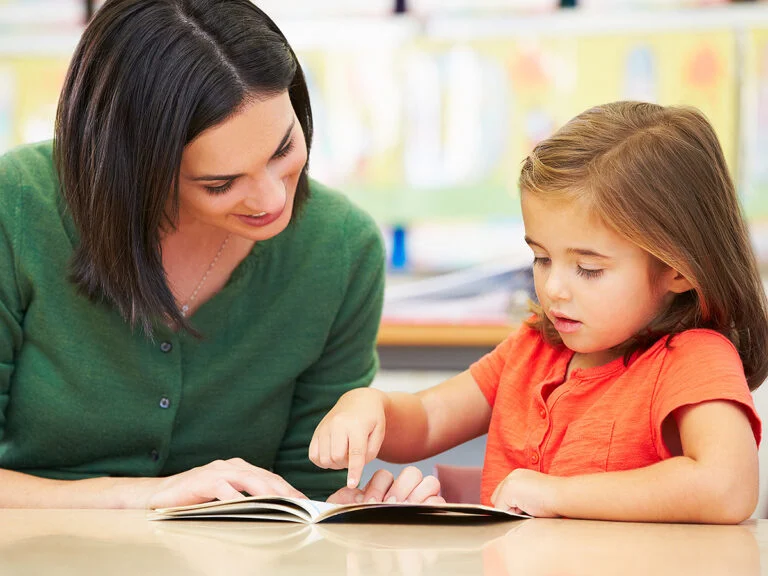 Young girl reading with teacher at school