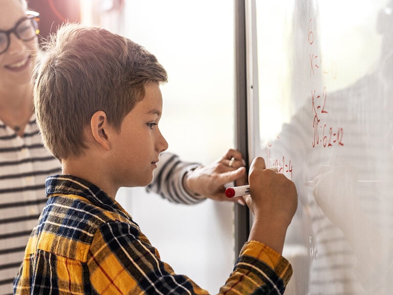 Young boy doing math on a whiteboard with teacher's help