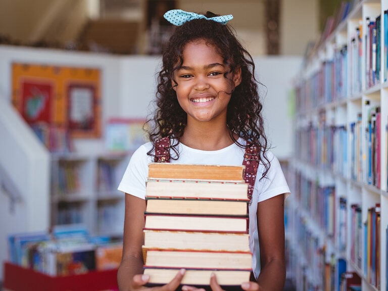 Portrait of smiling school girl carrying stack of books