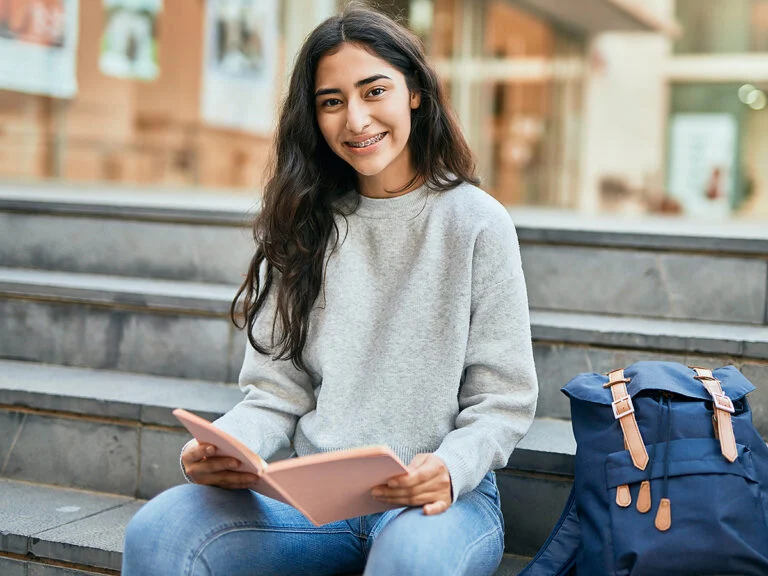 Middle school girl reading book on steps of school