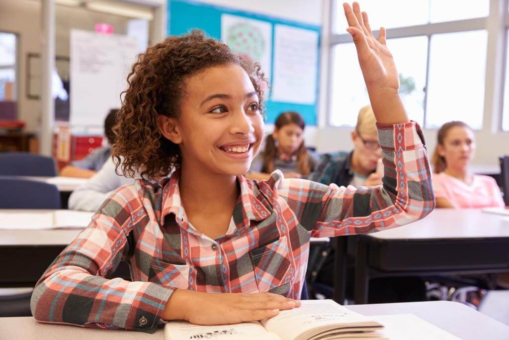 Schoolgirl at desk in elementary school raising her hand