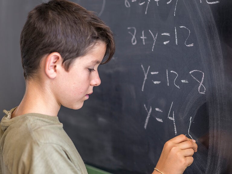 Male student solving algebra problem on a blackboard.