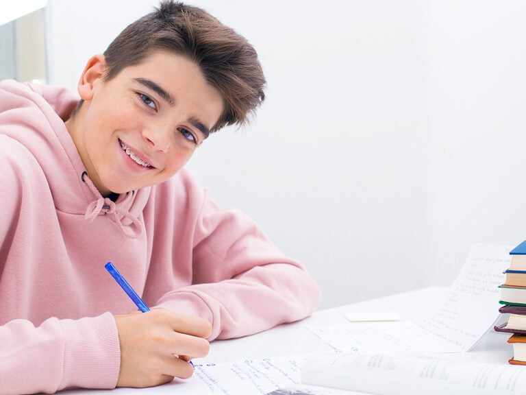 middle school age boy in pink hoodie studying at desk