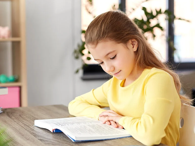 little student girl reading book at home