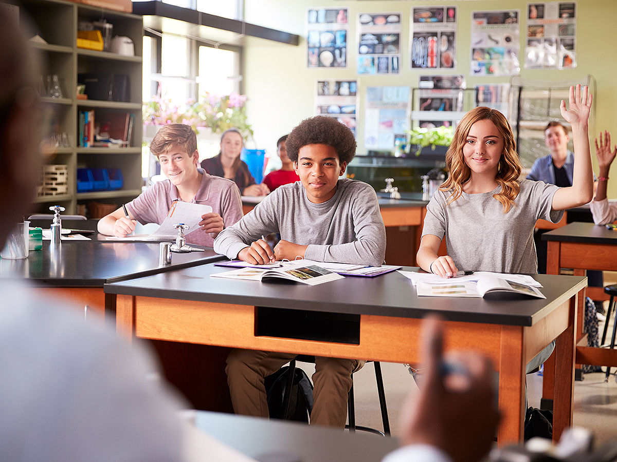 students in biology class, girl smiling and raising hand